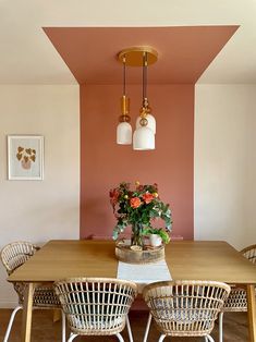 a dining room table and chairs with flowers in the center, against an orange painted wall