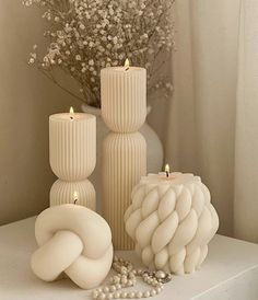 three white candles sitting on top of a table next to a vase filled with flowers