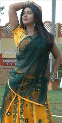 a woman in a yellow and green sari with her arms behind her head, posing for the camera