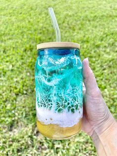 a hand holding a mason jar filled with blue and white liquid on top of green grass