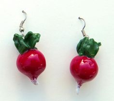 two red radishes with green leaves hang from hooks on a white surface,