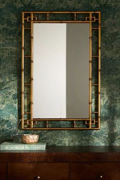 a mirror sitting on top of a wooden dresser next to a wallpapered wall