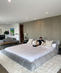 a man sitting on top of a large bed in a living room next to a couch