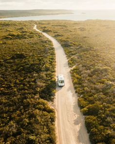 an aerial view of a truck driving down a dirt road in the middle of trees