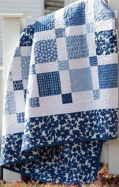 two blue and white quilts sitting on the back of a wooden chair in front of a house