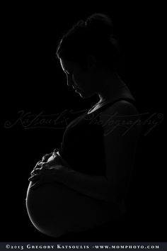 a pregnant woman standing in the dark with her hands on her stomach