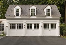 a white garage with three windows and two doors on the side of it, in front of some trees