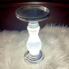 a glass candle holder sitting on top of a white fur covered floor next to a wooden table