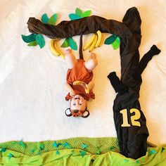 a child laying on top of a bed next to a fake tree with bananas hanging from it