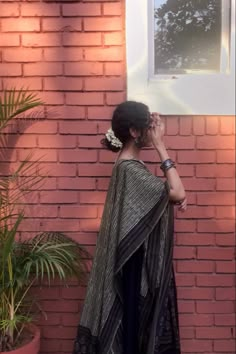 a woman standing in front of a brick wall wearing a black and silver sari