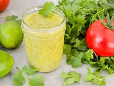 a glass jar filled with cilantro sauce next to tomatoes and limes