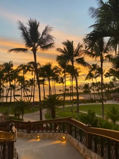 the sun is setting behind palm trees on the ocean front walkway to the beach at sunset