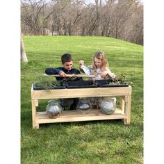 two children are sitting on a bench with plants in the middle and one child is holding an object