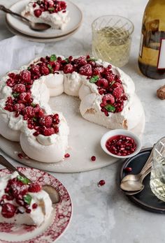 a cake with berries and whipped cream is on a table next to wine glasses, silverware and plates