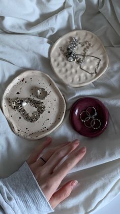 two white plates with rings on them sitting on a bed next to a person's hand