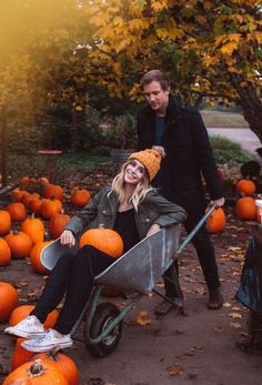 a man and woman sitting in a wheelbarrow surrounded by pumpkins