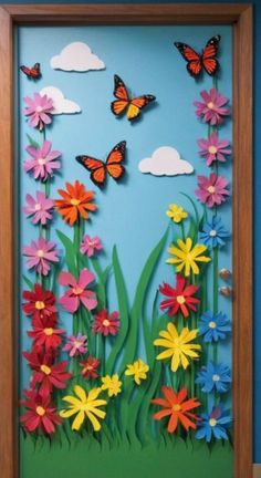 paper cut flowers and butterflies in the grass with blue sky behind them, on a wooden frame