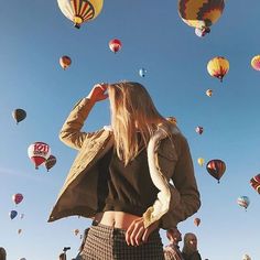 a woman is standing in front of many hot air balloons as she looks up at the sky