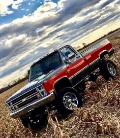 a red and black truck parked in a field next to a cornfield under a cloudy blue sky