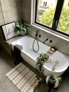 a bath tub sitting next to a window with plants on the floor and potted plants