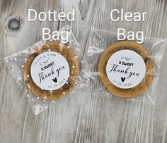 two cookies wrapped in plastic on top of a wooden table with thank you tags attached to them