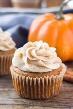 two cupcakes with frosting sitting on a wooden table next to pumpkins