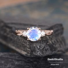 a ring with an oval blue stone surrounded by three smaller white stones on top of a rock