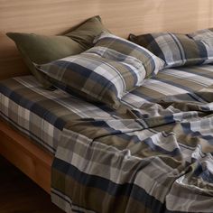 an unmade bed with plaid sheets and pillows