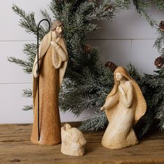 two figurines sitting on top of a wooden table next to a pine tree