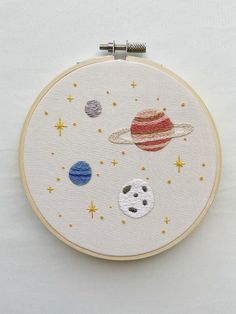 an embroidered space scene with saturn, pluto and other planets on white fabric in a hoop