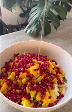 a white bowl filled with fruit on top of a wooden table next to a potted plant