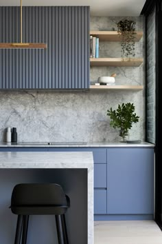 a modern kitchen with marble counter tops and blue cabinetry, along with a bar stool