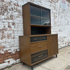 a wooden cabinet with glass doors and drawers on the outside of a brick building next to a sidewalk