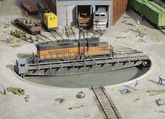 a model train station with several trains on tracks and people standing around the track area