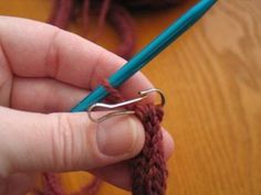 a person holding a blue crochet hook in their left hand and knitting yarn on the other