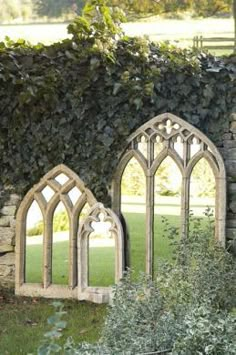 two stone windows sitting next to each other in front of a wall covered with ivy