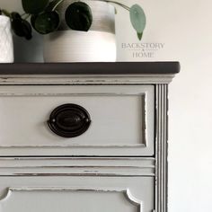 a white dresser with two potted plants on top and the words back story home above it