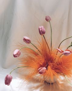 a vase filled with lots of pink flowers on top of a white table covered in feathers