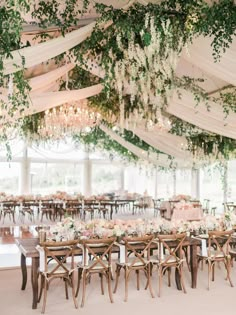 an elegant tented wedding reception with greenery and chandeliers hanging from the ceiling