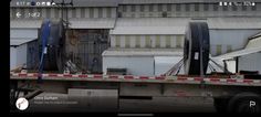 a flatbed truck is parked in front of an industrial building with large tires on it