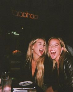 two beautiful young women sitting next to each other in front of a table with drinks