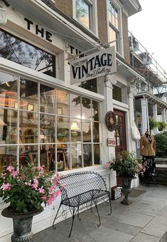 a store front with flowers in the window and a bench on the sidewalk next to it