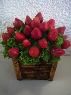 a wooden basket filled with lots of strawberries on top of a white table next to a wall