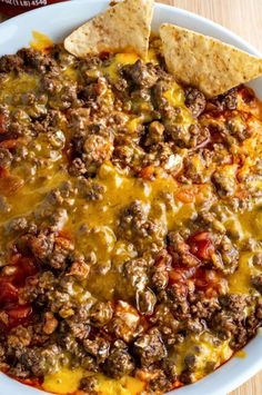 a white bowl filled with chili cheese and tortilla chips on top of a wooden table