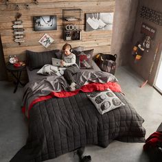 a young boy sitting on top of a bed in a bedroom next to a wooden wall