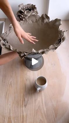 someone is making a vase out of clay on the table next to a coffee cup