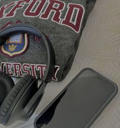 headphones, cell phone and pillow on a bed with the university t - shirt