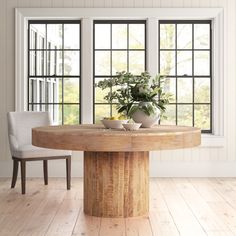 a wooden table with two chairs and a potted plant on it in front of large windows