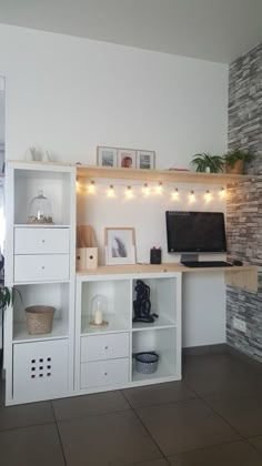 a computer desk with shelves and lights on the wall above it in a living room