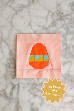 an orange piece of paper with the words egg design on it next to a pink envelope